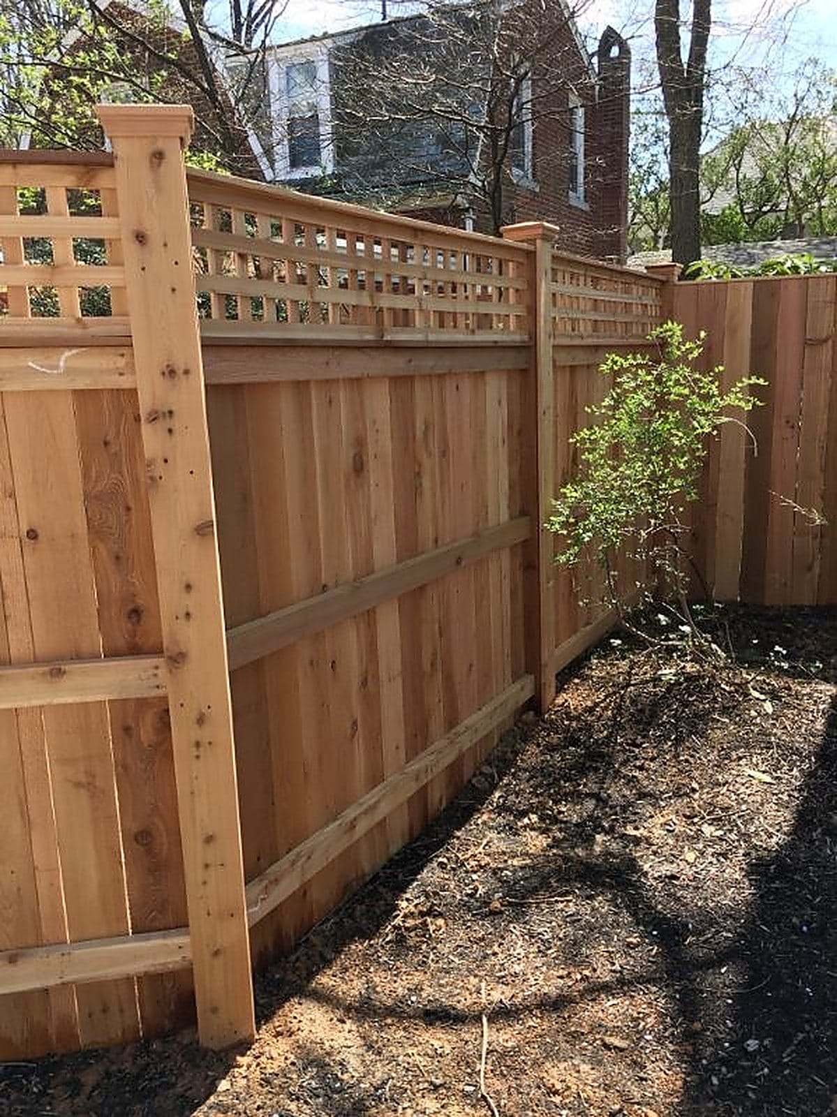 Cedar privacy fence with a square lattice topper running beside a brick house